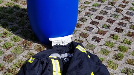 Bild einer Versuchsanordnung mit blauer Plastiktonne und Feuerwehrbekleidung  | © CRB Analyse Service GmbH